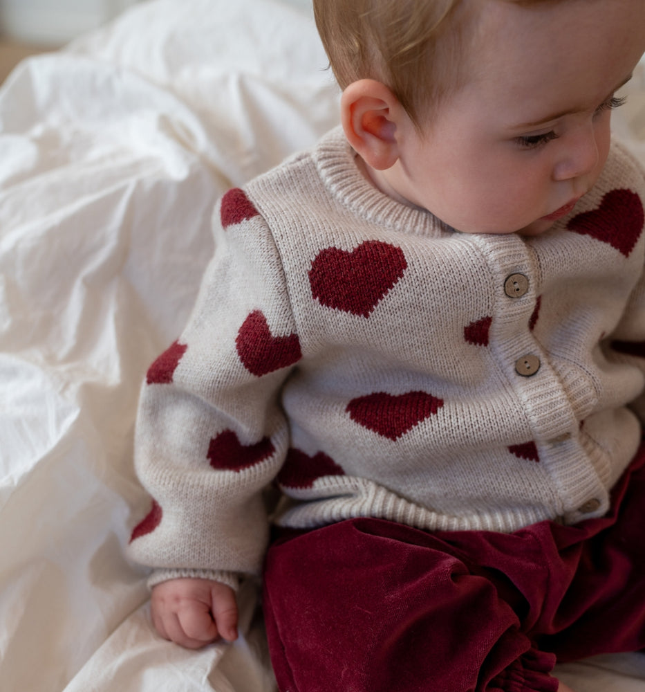 Baby i en cardigan med røde hjerter og røde bukser 